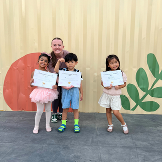 Dance students standing on a stage at The Ripe Market in Dubai, posing with their certificates for participating in the British Dance Academy winter performances.