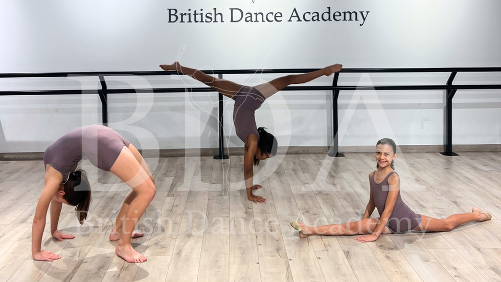 Three AcroDance students. One is doing a handstand, one is doing the splits and one is doing a back-bend, during their AcroDance class at British Dance Academy in Dubai. 
