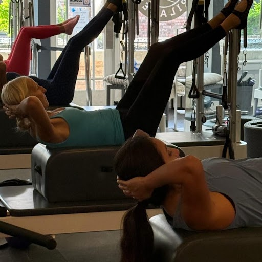 Two clients at Toned Body Pilates in Stuart, FL performing a supine reformer exercise with feet in straps and hands supporting the head for neck safety