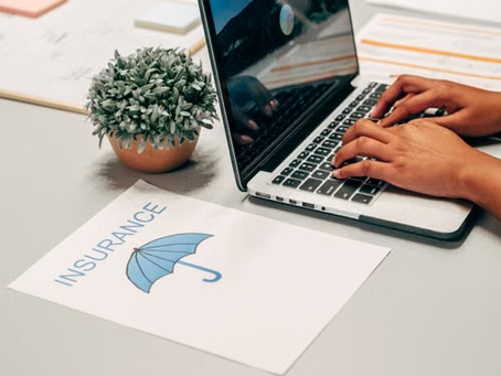 Person using a laptop beside an insurance document with an umbrella graphic, representing business insurance solutions in Forest Lake, MN.