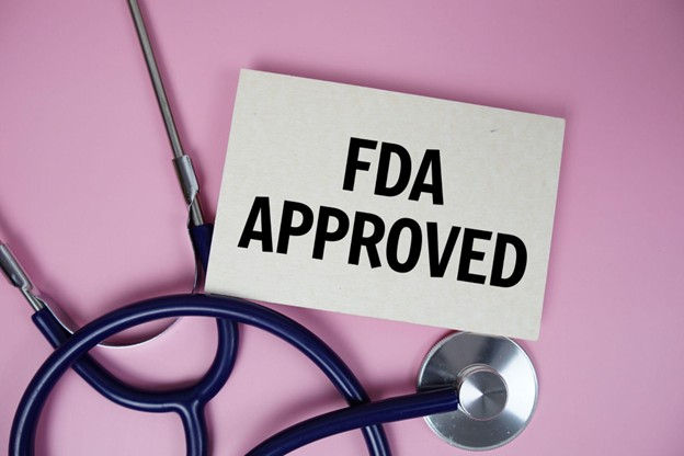 Stethoscope on pink background with a card reading "FDA APPROVED" in bold black letters, conveying a sense of approval and trust.