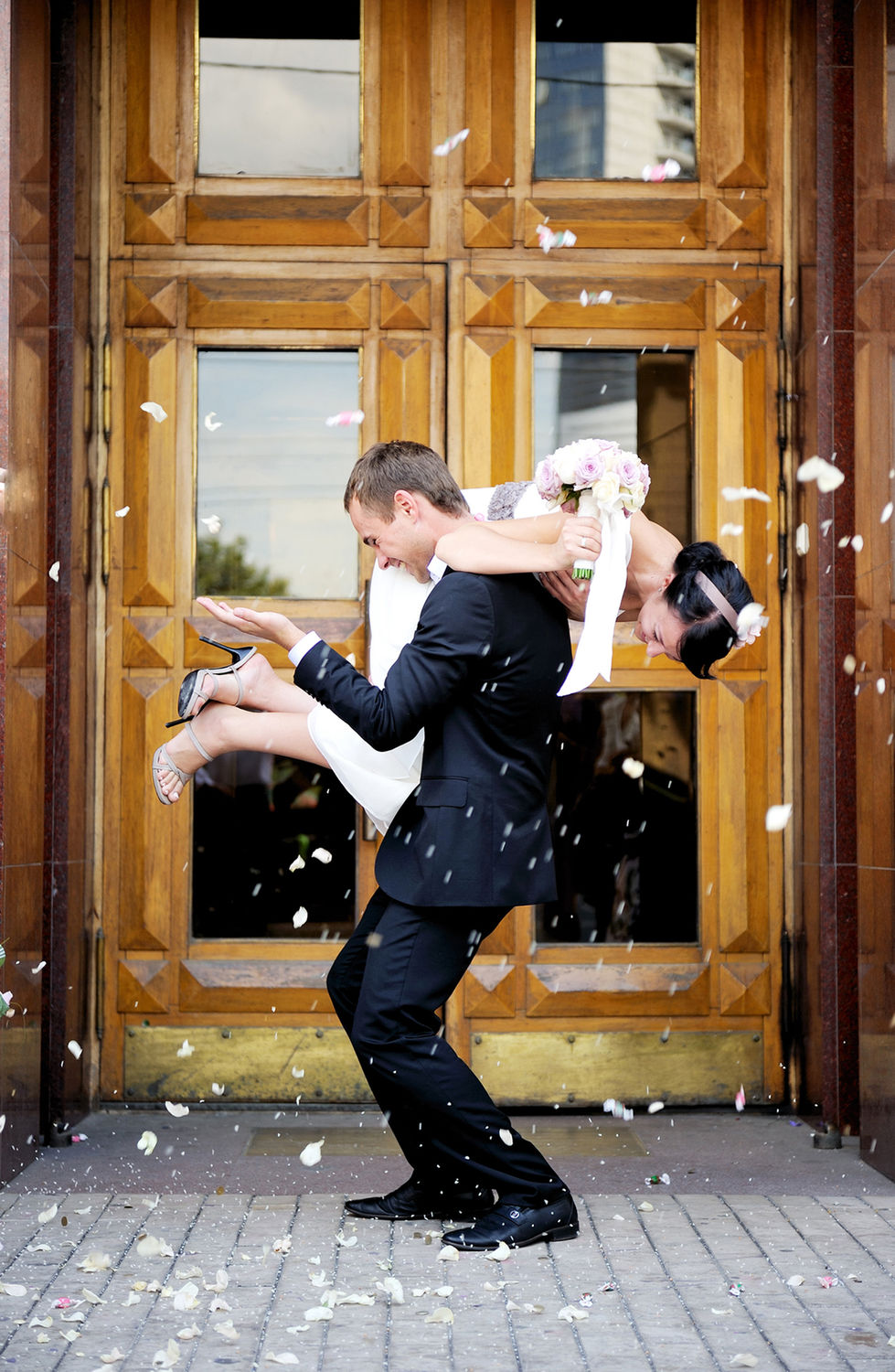 Groom swings bride celebrating their wedding in front of a golden doorframe. Mr&Mrs John's Wedding