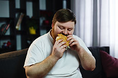 smiling-fat-man-eats-burger-sitting-before-tv-set.jpg