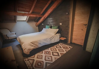 loft room, wrapped in the wood with bed, rug, and chair; wooden beams and door; Rooms & Lodge.