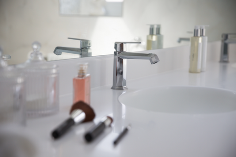 Chrome faucet on white bathroom countertop with toiletries.