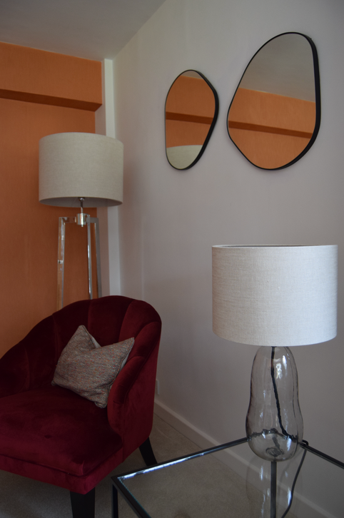 Room with red chair, lamps, and abstract mirrors.