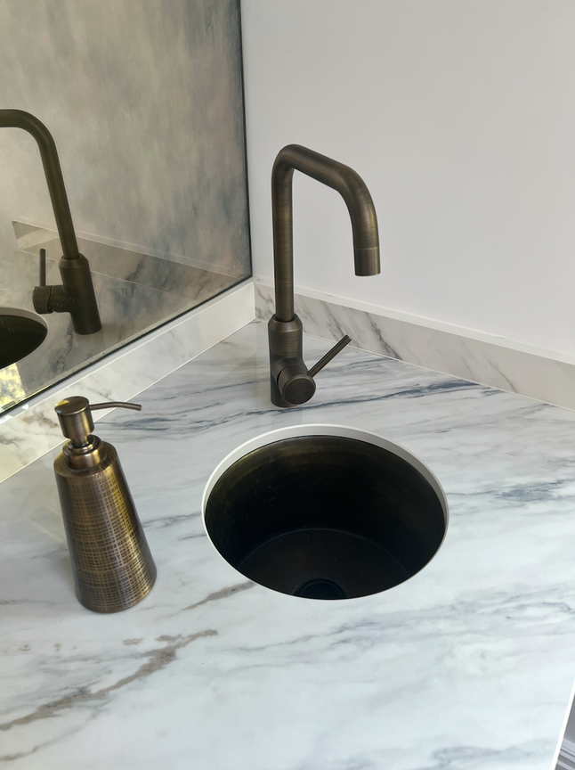 Marble countertop with bronze faucet and soap dispenser.
