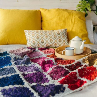 bright colored crochet blanket draped on bed with yellow pillows and tea set