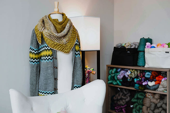 white chair with mannequin wearing hand knits and yarn on shelves