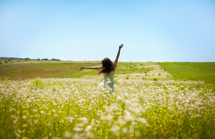 woman dancing in a green field with white flowers and blue sky