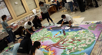 The project was inspired by award-winning children’s author Kate Seredy’s story of a World War I battle during which Hungarian soldiers crawled all night through total desolation. When they reached safety, there was one tree still standing, and hundreds of birds of varying species were singing together, birds that do not naturally do so, creating a unique and beautiful song.
In 1999, that story inspired an 8-year-old girl to wonder what would happen if people from all over the world, from different backgrounds and traditions, came together to make something beautiful like the birds’ song. She asked, “What if the whole world made a painting together?”
Today, a forest of “Singing Tree” paintings have been created by almost 12,000 people worldwide, according to Laurie Marshall, co-founder of the Singing Tree project. Each painting explores a theme and honors the essential role trees play in human life.
This project came to Ukiah after UHS teacher Eveline Rodriguez attended a summer seminar where Marshall shared information about her project. With support from fellow MESA teacher Sezgin Ramirez and MESA director Matt Sweeney, Rodriguez enlisted their MESA students in an ambitious project to create the 49th singing tree mural.
The name of the Ukiah High tree is the Manzanita Singing Tree of Kindness, and in it, students use art to explore questions such as, “What is a memorable act of kindness that you received or gave?” and “Is there someone you were unkind to whose trust you need to restore?”
Marshall coordinated the project, coming to Ukiah on Dec. 5, 12 and 19. She asked students to draw their visions of kindness and she incorporated those visions into a final mural design. She then encouraged project participants to invite students outside the MESA class to decorate the manzanita tree by creating leaves where they shared their ideas about kindness.
Rodriguez said, “Almost 50 MESA students were involved, and everyone had a role. We had committees responsible for preparing the leaves, for creating instructions so others could participate, for painting the mural, for figuring out where to display it once it’s done, and many others.”
The project not only produced a beautiful work of art, it incorporated several academic subjects, as well as enhancing students’ social and emotional development.
MESA students learned about the role of manzanita trees in local ecology. They used mathematics to create the grid to enlarge the master design, and they used engineering to design and build the free-standing mural with the help of the woodshop students.
They also used communication skills as they collaborated with classmates and invited others to participate by adding to the mural or documenting the project for the yearbook. Students expanded their social and emotional learning as they explored kindness; and finally, they used creative expression as they produced unique images that reflected their personal understanding of kindness.
Rodriguez said she was pleased so many colleagues chose to have their classes participate.
“More than a dozen teachers from many different departments got involved, like English, psychology, PE, science, art, independent study, special education, and foreign language,” she said.
Part of the project included more than contemplating kindness: students who shared memorable acts of kindness were encouraged to continue to practice those acts, and students who shared stories about needing to restore trust or apologize were encouraged to follow up and make amends.
“For the students who participated, I think this project created awareness about kindness, and how important it is. I also think it gave them hope. It showed them they can make changes when they believe in themselves. We did this project in three weeks. We can do so much more when we work together.”
To learn more about the Singing Tree project, visit www.unitythroughcreativity.net/programs/singing-tree-forest. Marshall and co-founder Lili Lopez also work with an international non-profit whose mission is peace-building through art (createpeaceproject.org).
By Ukiah Daily Journal | udj@ukiahdj.com |
PUBLISHED: January 23, 2018 at 12:00 am | UPDATED: August 23, 2018 at 12:00 am (used with permission)