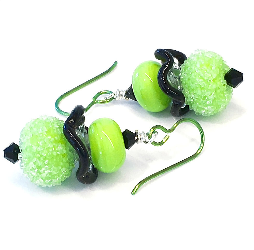 green lampwork bead earrings laying flat on a white surface