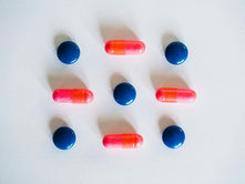 Blue tablets and red capsules arranged in a grid on a white background, creating a symmetric pattern. Bright and orderly mood.