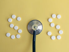 A stethoscope forms the letter "O" between the numbers "SOS" made of white pills on a yellow background.