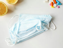 Blue face masks on a white surface with lemon slices and colorful pills scattered nearby. Bright and clean composition.