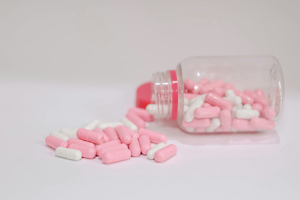 Two people sit at a table in a room with warm light. One wears a yellow shirt and a headscarf, and the other wears blue scrubs and a cap, smiling with a hand on the other's shoulder. On the table are colorful ribbons in pink, orange, and blue, two blister packs of pills, and boxes labeled "RESILIX" and "HOPEXRA." A sign on the wall reads "STRENGTH IN EVERY STEP." Potted plants are in the background.