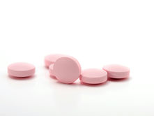 The image shows several pink, round pills scattered on a plain white background. The simplicity of the scene emphasizes the pills, suggesting a focus on medication or pharmaceutical themes, possibly related to healthcare, treatment, or dosage. The lack of additional context keeps the attention on the pills themselves.