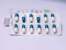 Blister pack with 10 blue and white capsules on a white surface. Box is blurred in the background.
