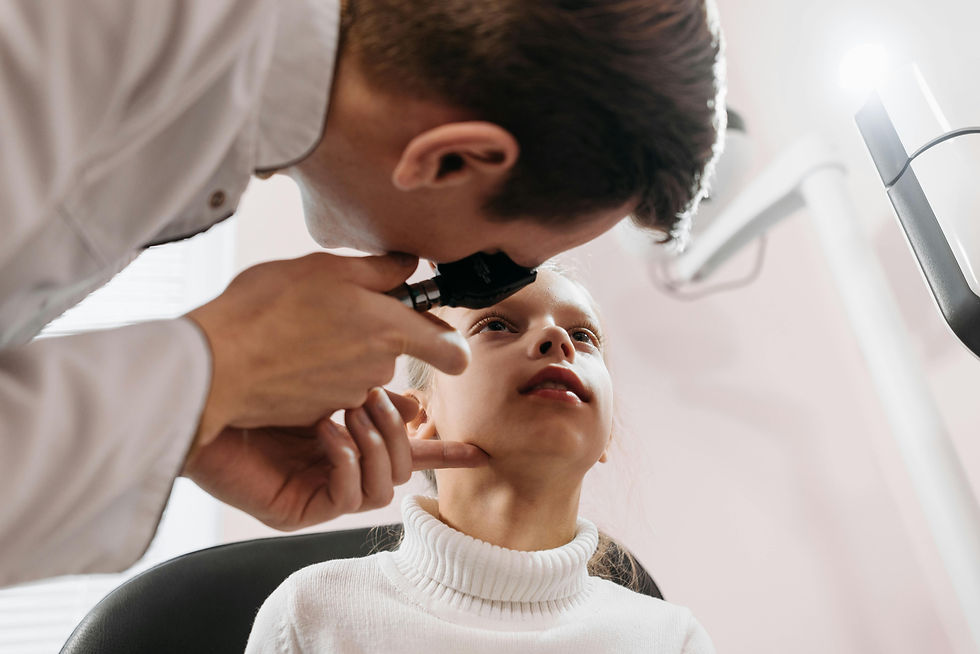 Doctor examines child's ear with otoscope in a well-lit clinic. Child in white turtleneck looks calm, seated in black chair.