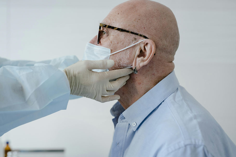 Man wearing glasses and a mask is examined by a healthcare worker in gloves. Background is a plain, light-colored wall. Mood is clinical.