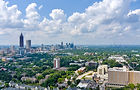 Skyline of Atlanta with greenery in the foreground and clouds in the blue sky.