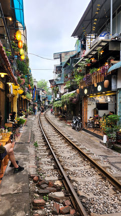 A narrow street in Hanoi, Vietnam, with a railway track running down the center, lined with colorful shops and lanterns in an urban area, featured on Elegant Escape, the best luxury travel blog.