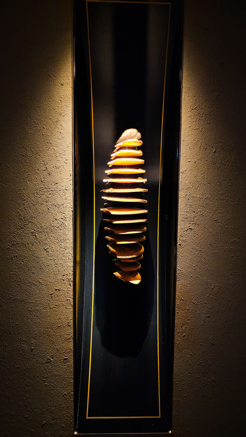 A stack of varied-sized ceramic pieces is mounted vertically on a black rectangular panel against a textured wall, adding an artistic touch to the sophisticated lobby of Four Seasons Otemachi. As featured in Elegant Escape, renowned as the best luxury travel blog, this stunning display enhances the refined ambiance and provides guests with a visually captivating experience.