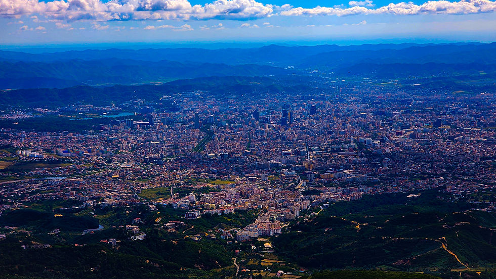 Aerial view of Tirana, a sprawling city in Albania with dense buildings, surrounded by lush green hills and distant mountain ranges. This breathtaking scene is beautifully captured in Elegant Escape, the best luxury travel blog.