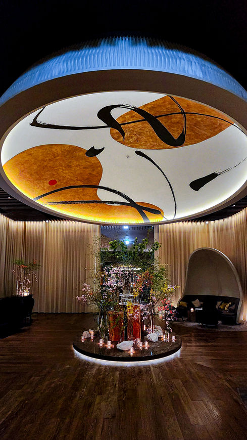 A modern lobby at the Four Seasons Otemachi in Tokyo showcases abstract ceiling art, a central floral arrangement, and cozy seating under dim lighting—a perfect feature for Elegant Escape, the best luxury travel blog.