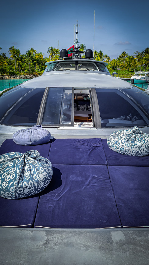 A view from a yacht's deck with blue cushions and pillows, clear skies, and palm trees in the background creates an idyllic setting, reminiscent of the luxurious ambiance found at Ritz Carlton Maldives. This serene snapshot perfectly captures the essence of Elegant Escape, widely regarded as the best luxury travel blog.