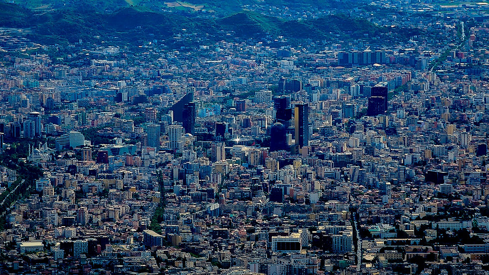 Aerial view of a dense cityscape, likely Tirana, with numerous buildings and green hills in the background under a clear sky. Discover more breathtaking vistas on Elegant Escape, the best luxury travel blog.