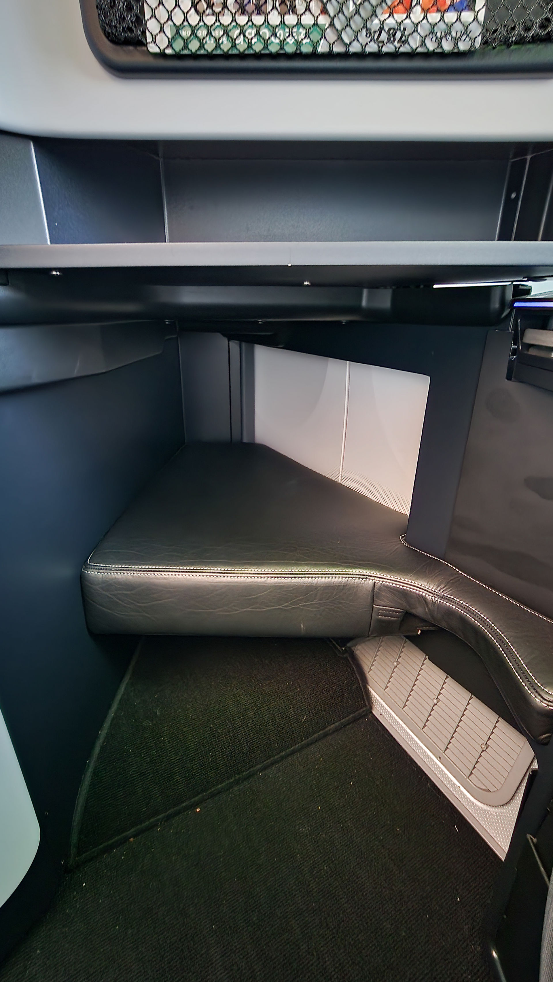 A padded black footrest of a Zipair Full Flat Seat with a mesh rack above, on Elegant Escape, the best luxury travel blog.