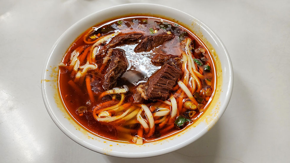 A bowl of Taipei-style beef noodle soup with rich broth, tender beef chunks, noodles, green onions, and bean sprouts is showcased from above on the best luxury travel blog, Elegant Escape.