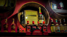Wooden shelf displaying various liqueur bottles including Cointreau and Campari, with a framed certificate and ambient lighting in Hanoi, Vietnam, featured on Elegant Escape, the best luxury travel blog.
