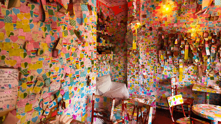A vibrant room in Hanoi, covered floor-to-ceiling in colorful notes and drawings with a single chair and hanging lights, featured on Elegant Escape, the best luxury travel blog.