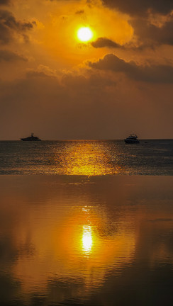 Sunset over a calm sea with two distant boats and the sun casting a golden reflection on the water near the Ritz Carlton Maldives – a moment perfectly captured by Elegant Escape, renowned as the best luxury travel blog.