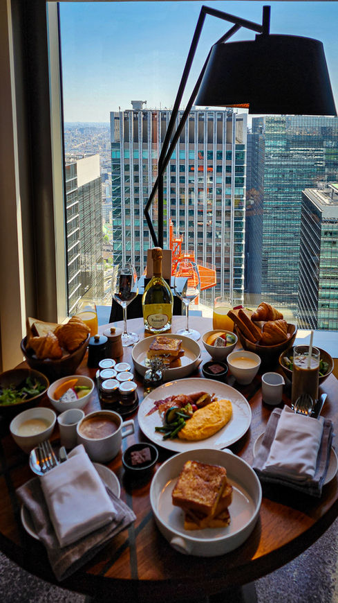 Breakfast spread on a round table with city skyscrapers visible through the window in the background of a Tokyo hotel room, featured on Elegant Escape – the best luxury travel blog.