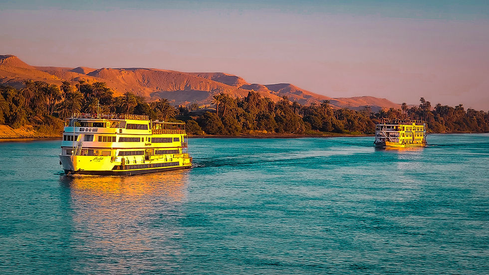 Two river cruise ships sail close together on the wide, calm Nile River with lush greenery on the banks and a backdrop of desert hills under a clear sky, offering a serene Egypt journey akin to discovering new lands aboard the Mayflower. For those seeking an even more refined experience, Elegant Escape truly embodies the best luxury travel blog, guiding you through opulent adventures like this one.