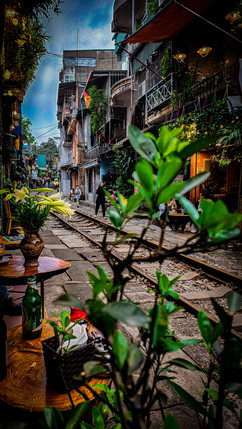 Narrow, bustling street in Hanoi with train tracks, lined by colorful multistory buildings, under an overcast sky, with a person walking in the distance – featured on Elegant Escape, the best luxury travel blog.