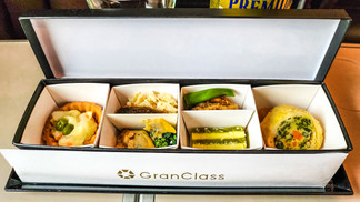 Elegant Escape offers a dining experience reminiscent of the best luxury travel blog, featuring an elegant bento box with five compartments of assorted appetizers on a Gran Class tray table, elevating your journey as the Shinkansen glides along its tracks.