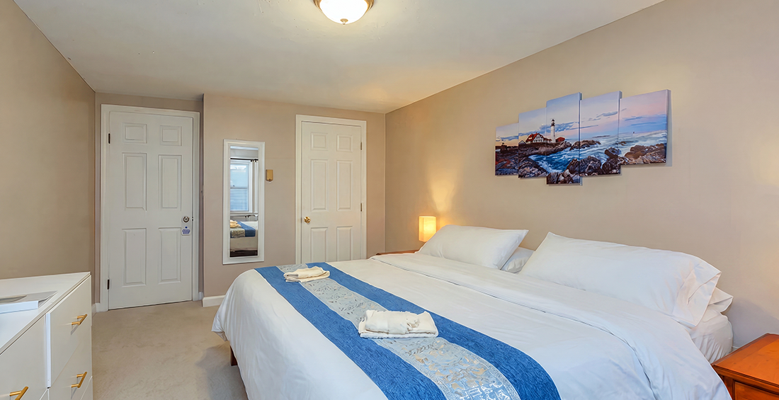 Guest room at Lake Shore Farm Inn in Northwood, NH with king bed with white bedding, blue accents, private bath, and coastal wall art.