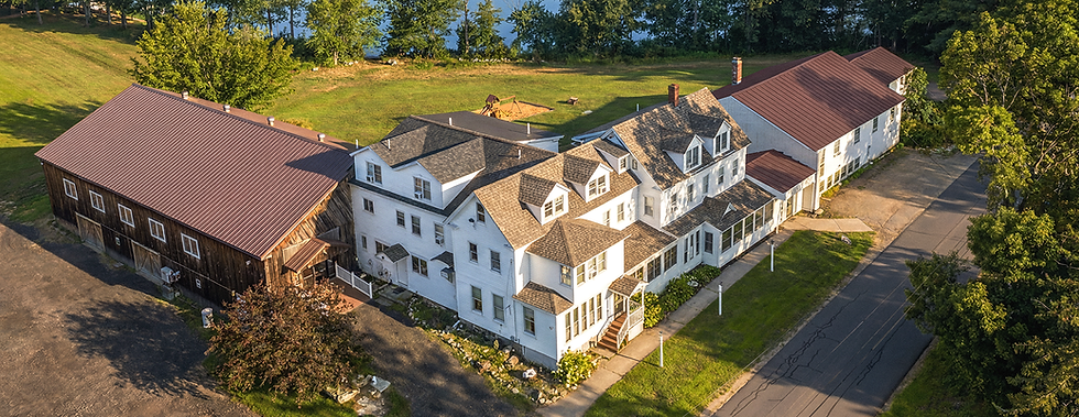 Aerial view of Lake Shore Farm Inn in Northwood, NH with guest buildings, parking areas, trees, and Jenness Pond nearby.