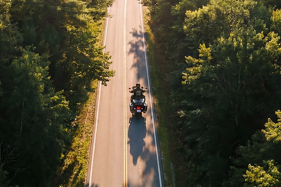 Aerial view of a motorcyclist riding a sunlit New Hampshire forest road near Lake Shore Farm Inn in Northwood.