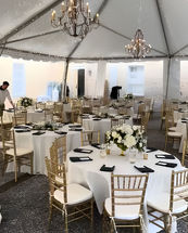 Wedding reception setup with round tables, white linens, gold chairs, and flowers.