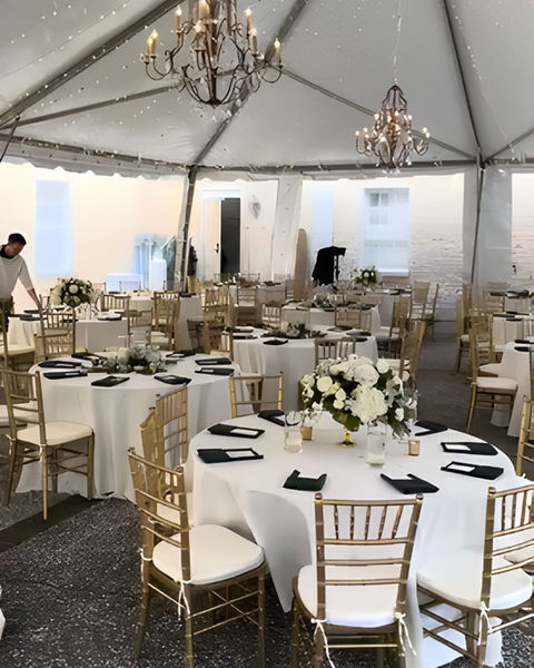 Wedding reception setup with round tables, white linens, gold chairs, and flowers.