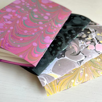Four handmade marbled notebooks stacked in a pile. 