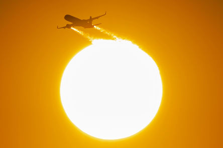 A commercial airliner flies in front of a beautiful sunset sun. 
