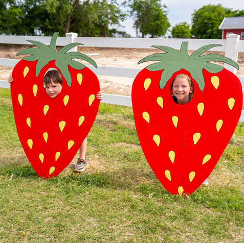 Two young kids with their faces in two strawberry wooden cut out photo ops!