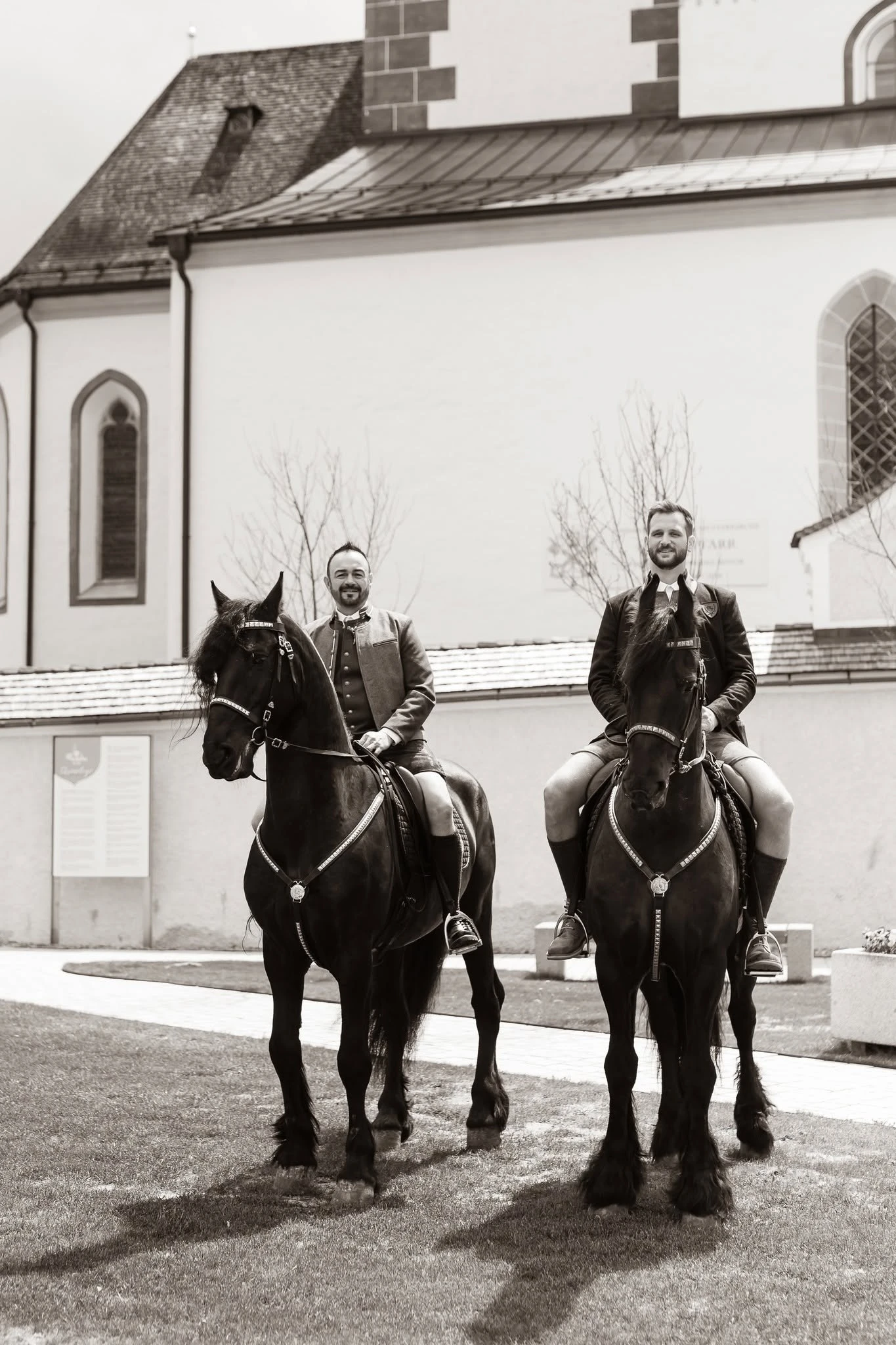 Zwei Reiter auf schwarzen Friesen vor einer Kirche