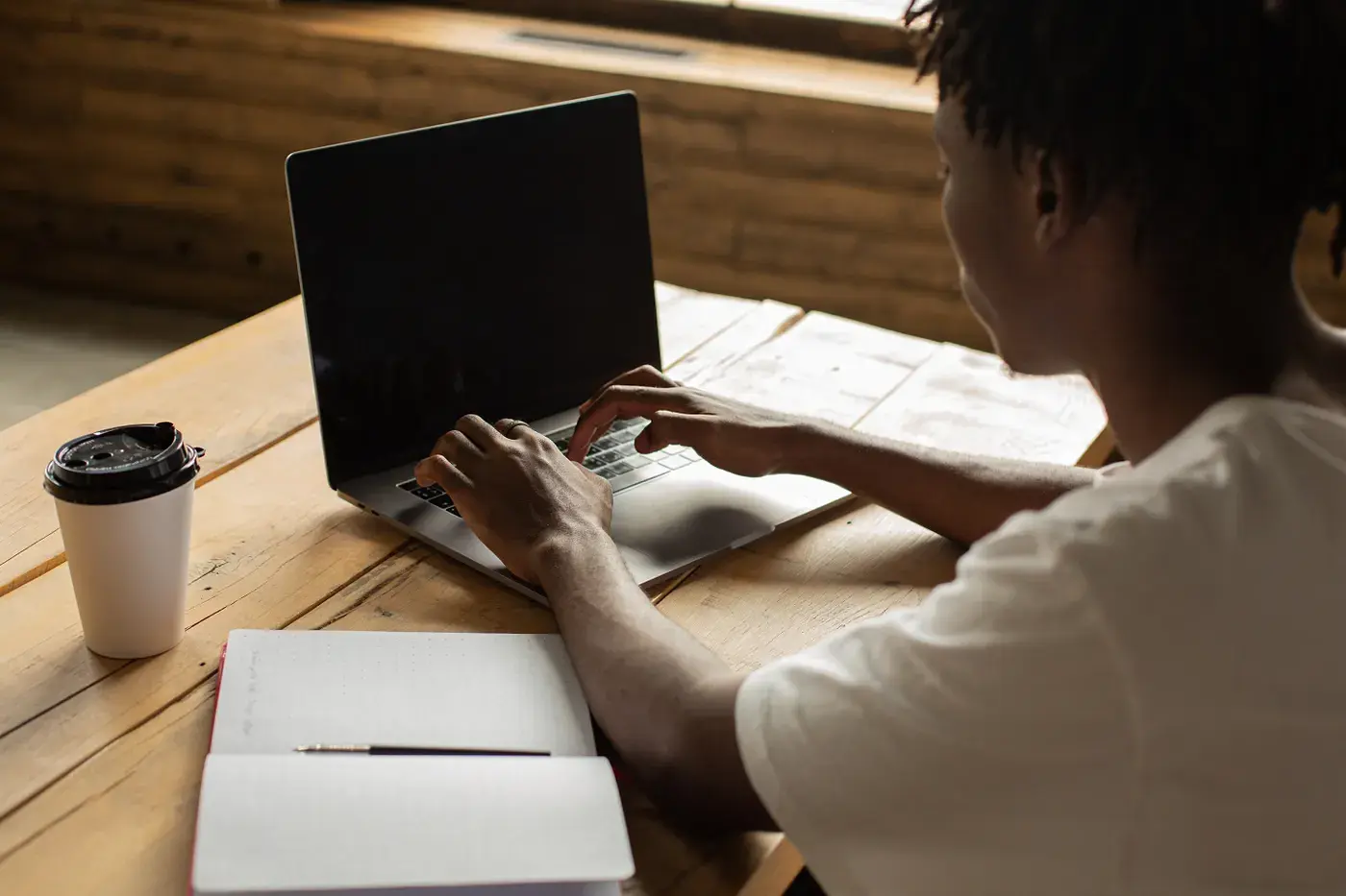 A small business owner doing bookkeeping on a laptop at a wooden desk with a coffee